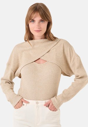 Top beige a maniche lunghe con texture a coste, design avvolgente asimmetrico e scollatura aperta sul petto; abbinato a pantaloni bianchi a vita alta.