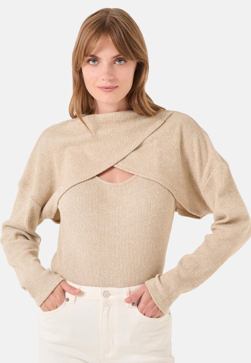 Top beige a maniche lunghe con texture a coste, design avvolgente asimmetrico e scollatura aperta sul petto; abbinato a pantaloni bianchi a vita alta.