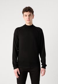 Haut à manches longues noir en tissu tricoté, avec un col haut et des manches raglan, doté d'une texture lisse et d'une coupe ajustée.