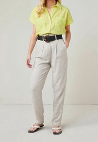 Lichtgroen shirt met korte mouwen en twee zakken, gecombineerd met lichtgrijze geplooide broek met een subtiele streep. Zwarte gestructureerde riem met een ronde gesp.