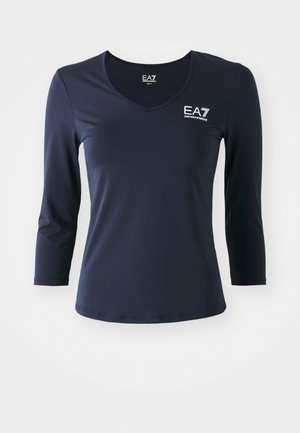 Tamsiai mėlynas ilgas rankovėmis viršus su V formos iškirpte, pagamintas iš lygaus audinio. Su EA7 logotipu ant krūtinės ir prigludusia forma, turi paprastą, švarų kirpimą.