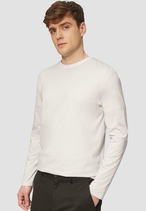Camiseta de manga larga blanca hecha de algodón suave. Diseño de cuello redondo con una textura ligera. Combinada con pantalones oscuros. Estilo simple y minimalista.