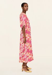 Rochie lungă roz cu flori, cu mâneci scurte voluminoase, având modele de frunze portocalii și albe; asortată cu pantofi cu toc joasă aurii.