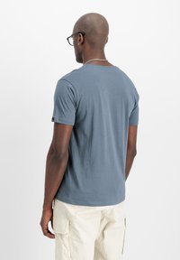 Graues Kurzarm-T-Shirt mit rundem Ausschnitt, glatter Textur und einem dezenten Logo am Ärmel; kombiniert mit hellen Cargo-Hosen.