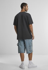 Grijze katoenen t-shirt met een ontspannen pasvorm, gecombineerd met lichtblauwe denim shorts met een cargozak en witte sneakers.