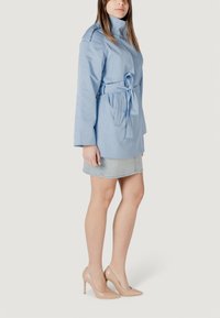 Trench coat belted di un azzurro chiaro con un colletto alto e maniche lunghe, abbinato a una gonna di jeans e tacchi alti color nude.