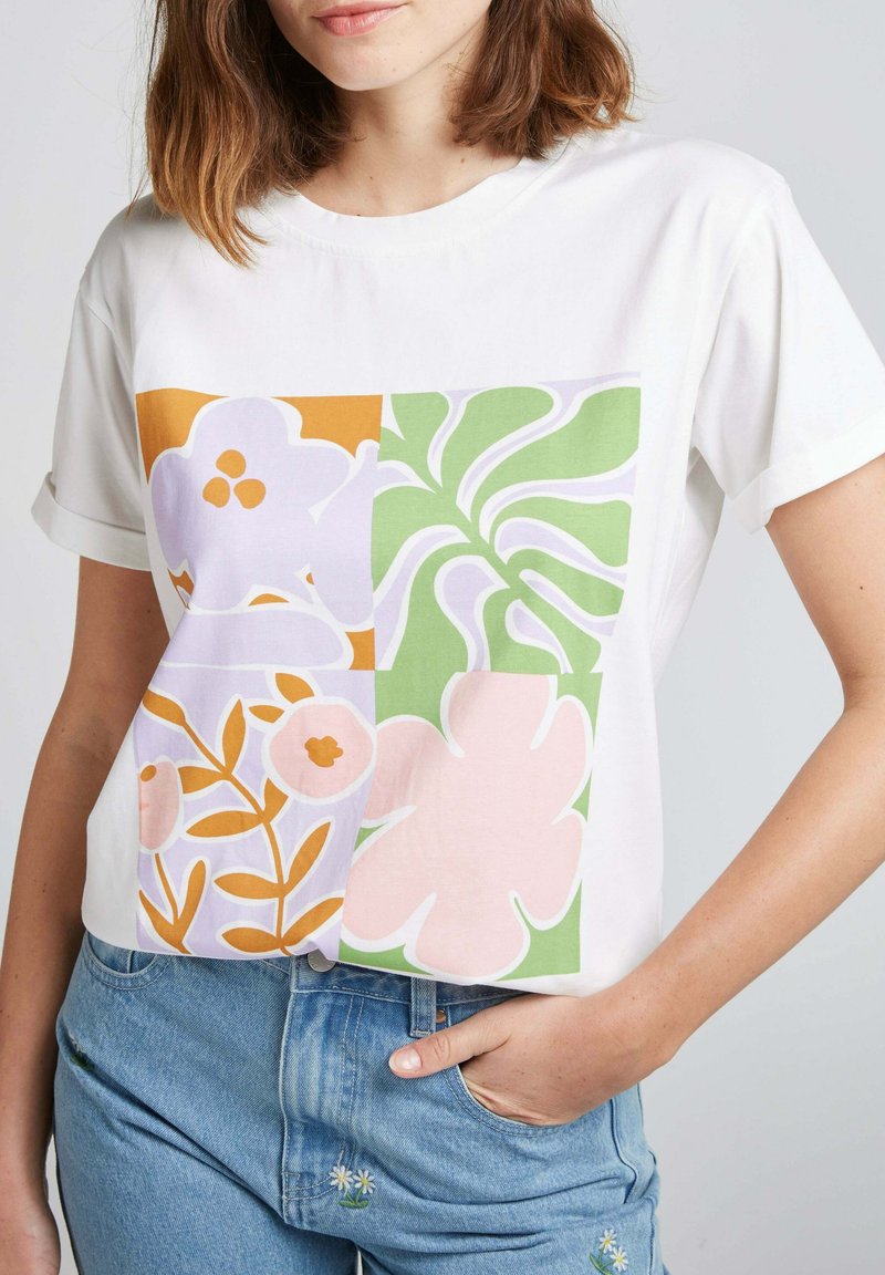 T-shirt blanc à manches courtes présentant un imprimé floral dans des couleurs pastel : violet, orange, rose et vert, avec des formes et des designs variés.
