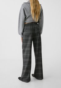 Harmaa lyhyt neule, yhdistetty mustiin ja harmaisiin ruudullisiin leveälahkeisiin housuihin, joissa on joustava vyötärö ja suora leikkaus. Sileä kangaspinta.