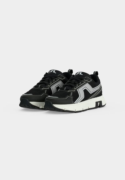 Paire de chaussures de sport noires et blanches avec empeigne en mesh, semelles blanches épaisses et accents argentés réfléchissants, vues de profil, de face.