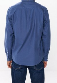 Niebieska koszula na guziki z długimi rękawami, wykonana z gładkiego materiału, z karczkiem z tyłu i zapięciem na guziki przy mankietach. Nosi się ją z ciemnymi dżinsami.