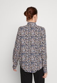 Blusa floreale a maniche lunghe con una combinazione di fiori blu, rosa e bianchi su uno sfondo nero. Collo a rotondo e orlo leggermente curvato.