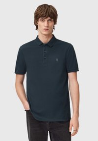 Dunkelblaues Polohemd mit klassischem Kragen, dreiknöpfiger Knopfleiste und kleinem gesticktem Logo auf der linken Brust. Weicher Baumwollstoff.