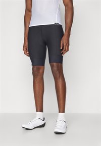 Schwarze Radshorts mit einem figurbetonten Design, ausgestattet mit einem kontrastierenden, glatten Taillenbund und strukturiertem Stoff. Getragen mit einem atmungsaktiven weißen Oberteil.