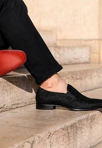 Zwarte instapschoenen met een gestructureerd oppervlak en een gladde afwerking, met een lage hak en zonder zichtbare veters, gepresenteerd op stenen trappen.