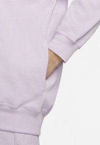 Levandulový svetr s žebrovaným lemem a boční kapsou. Měkká, strukturovaná tkanina zvýrazňuje uvolněný střih a ležérní design.