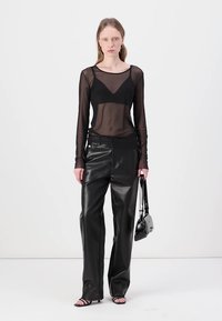 Svart transparent långärmad topp, figurnära med V-hals; kombinerad med högmidjade svarta läderbyxor med vida ben; liten handväska och sandaler med remmar.