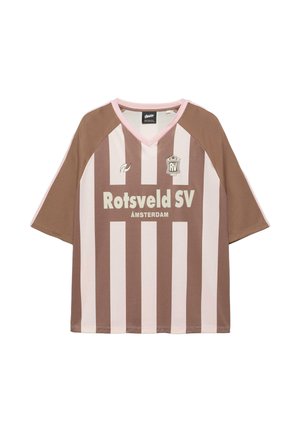 Ung mand iført brun og pink stribet sportstrøje, lange denimshorts med synlig tekst, hvide sokker med sorte striber og brune sko.