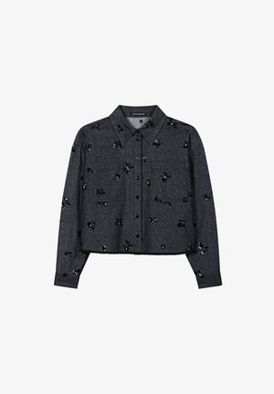 Cropped grey shirt with a collared neckline, featuring black sequin floral embellishments and two front pockets. Button closure.