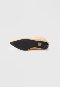 Beige nubuck peke støvlett med spiss tå ligger på siden og viser den svarte sålen med en rugglet oval grep og liten hæl.