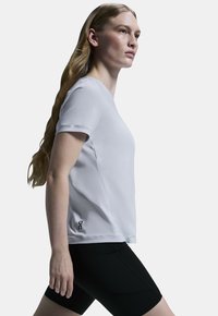 Vit sporttröja i lättviktigt material med korta ärmar. Har en svart logotyp på vänster sida, kombinerad med svarta shorts.