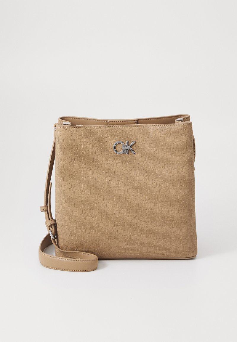 Tan crossbody torba z vzorcem v odtisu, srebrno kovinsko logo opremo in nastavljivim trakom. Pravokotna oblika z gladko teksturo.