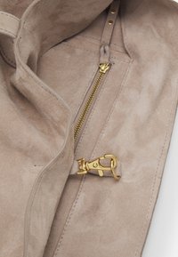 Intérieur de sac en suède marron clair avec une poche zippée dorée et un fermoir homard doré attaché à une sangle.