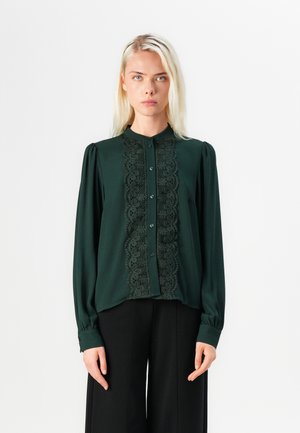 Dark green blouse featuring a front lace panel, button closure, and long sleeves with fitted cuffs. Smooth fabric in a relaxed fit.
