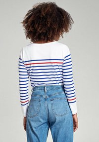 Witte lange mouwen top met horizontale blauwe en rode strepen; gecombineerd met lichtblauwe high-waisted denim jeans met achterzakken.