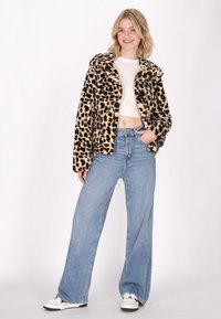 Jachetă din imitație de blană cu imprimeu de leopard, cu guler tăiat, purtată cu blugi blue light cu picioare largi și adidași albi.