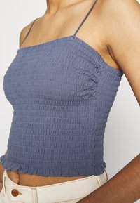 Top corto blu arricciato con spalline sottili, caratterizzato da una texture gather e un orlo a volant. Realizzato in tessuto leggero.