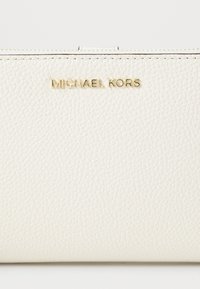 White textured leather wallet with a gold "Michael Kors" logo on the front, featuring a zipper closure and smooth stitching details.