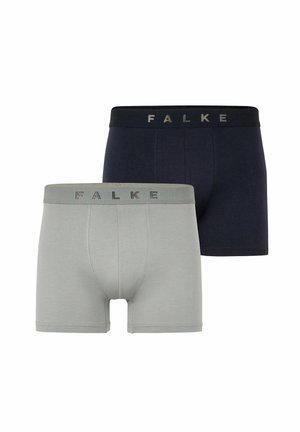Hemdloser Mann steht barfuß, trägt dunkelblaue eng anliegende Boxershorts mit FALKE-Logo am Bund vor einem schlichten weißen Hintergrund.