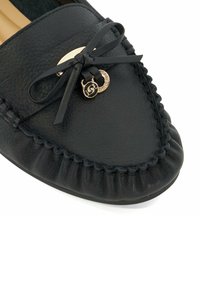 Zwarte leren moccasinschoen met een ronde neus, voorzien van een strik en een gouden accent met logo-detail; met gestructureerde stiksels rondom de rand.