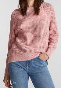 Lichtroze gebreide trui met een textuurpatroon, geribde halslijn en zoom, gecombineerd met blauwe jeans. Ontspannen pasvorm en lange mouwen.