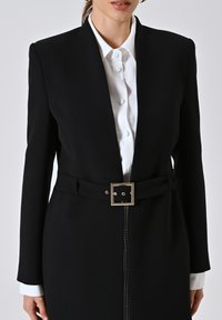 Abito blazer nero con scollatura profonda, maniche lunghe e silhouette aderente. Presenta una cintura abbinata con una fibbia quadrata dorata.