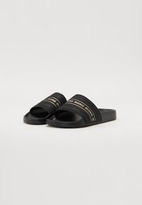 Svart slidesandaler med tykke, teksturerte stropper som har et gjentagende logo-mønster og en flat gummisåle for komfort.
