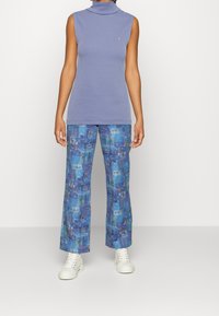 Lila ärmlös topp med hög krage, kombinerad med blå mönstrade vida byxor med abstrakta mönster. Vita platta sneakers fulländar looken.