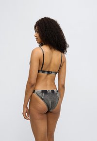 Σετ γυναικείας εσώρουχης δύο τεμαχίων σε μαύρο και γκρι, με ρυθμιζόμενες τιράντες. Ομαλή υφή, μινιμαλιστικός σχεδιασμός, με οπίσθια όψη.