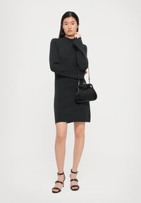 Fekete kötött ruha magas nyakkal és hosszú ujjakkal, kiegészítve egy kicsi fekete krokodilbőr mintás kézitáskával és pántos fekete magassarkú cipővel.