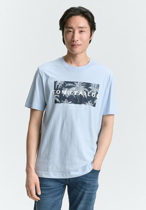 Camiseta de algodón azul claro con un estampado gráfico que presenta palmeras y el texto "TOM TAILOR" en blanco sobre un fondo oscuro.
