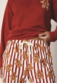 Röd långärmad tröja med en pepparkaksfigur-påse; pyjamasbyxor med bruna pepparkaksfigurer och vita ränder, knutna med ett vitt dragsnöre.