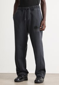 Dark grey sweatpants with elastic waistband, side pockets, and a black rectangular Hugo logo on the front. Loose fit and smooth fabric texture.