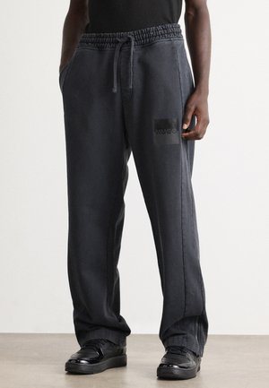 Dark grey sweatpants with elastic waistband, side pockets, and a black rectangular Hugo logo on the front. Loose fit and smooth fabric texture.