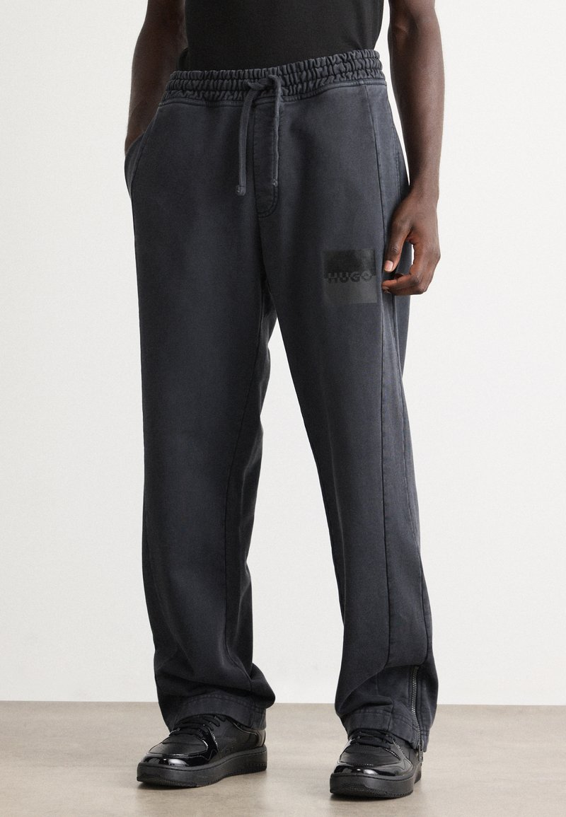 Dunkelgraue Jogginghose mit elastischem Bund, Seitentaschen und einem schwarzen rechteckigen Hugo-Logo auf der Vorderseite. Lockere Passform und glatte Stofftextur.