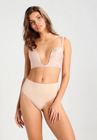 Nude spalvos apatinio trikotažo rinkinys, kuriame yra gilios iškirptės liemenėlė su plonomis petnešėlėmis ir aukšto liemens kelnaitės. Lygus tekstūra ir nesiūtas dizainas.