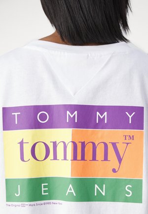 Hvid t-shirt med et multicolor logo design, hvor "TOMMY" er i lilla, "tommy" i orange, og "JEANS" i hvid på en grøn baggrund.