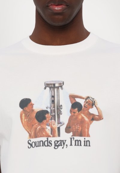 Póló, amin négy ing nélküli férfi grafikája van, akik egy szabadtéri zuhany körül gyűltek össze, és alattuk a "Sounds gay, I'm in" felirat.
