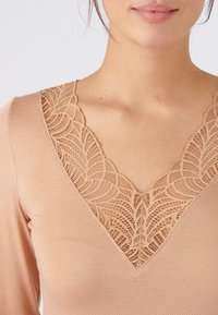 Maglia a maniche lunghe color beige chiaro con scollatura a V, caratterizzata da un delicato accento in pizzo all'escursione del collo, texture del tessuto liscia e design aderente.