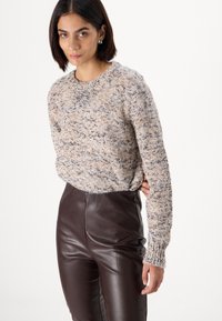 Pull en tricot en tissu marlé beige et marron, col rond, manches longues, associé à un pantalon en faux cuir marron taille haute.