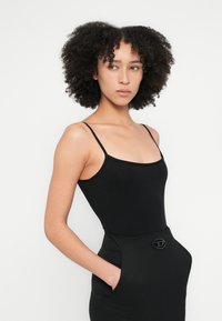 Fekete, ujjatlan body vékony pántokkal, karcsúsított szabás és sima textúra; magasított derekú szoknyával párosítva, amely zsebbel és díszítő fémrátéttel rendelkezik.